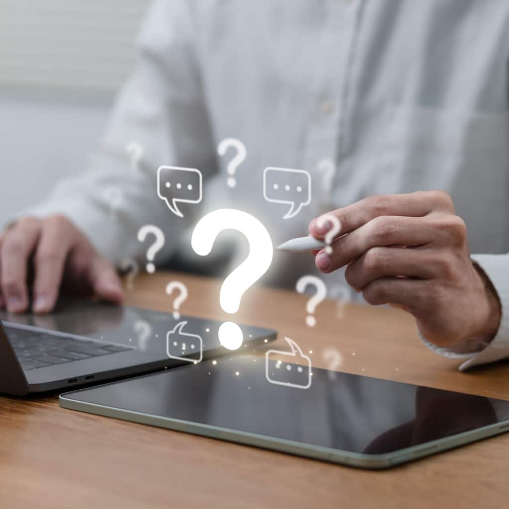 Questions & Support Client : Consultation Numérique Main tenant un stylet blanc devant un point d'interrogation lumineux entouré de bulles de dialogue, travaillant sur ordinateur portable et tablette.